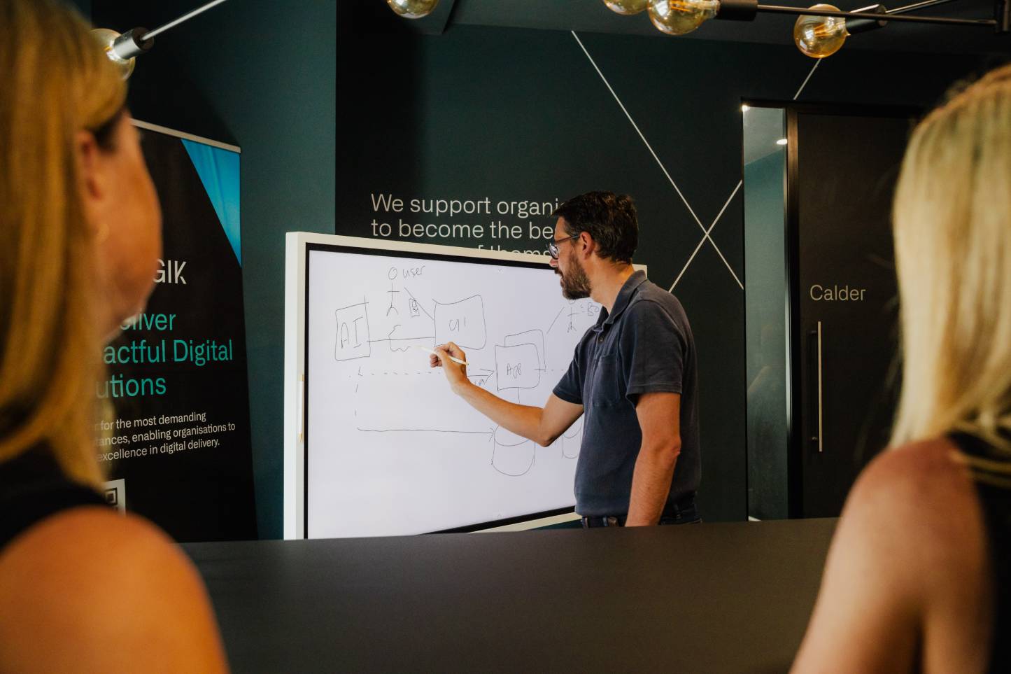 An architect sketching a system diagram of AI, UI and app components on a whiteboard while colleagues watch